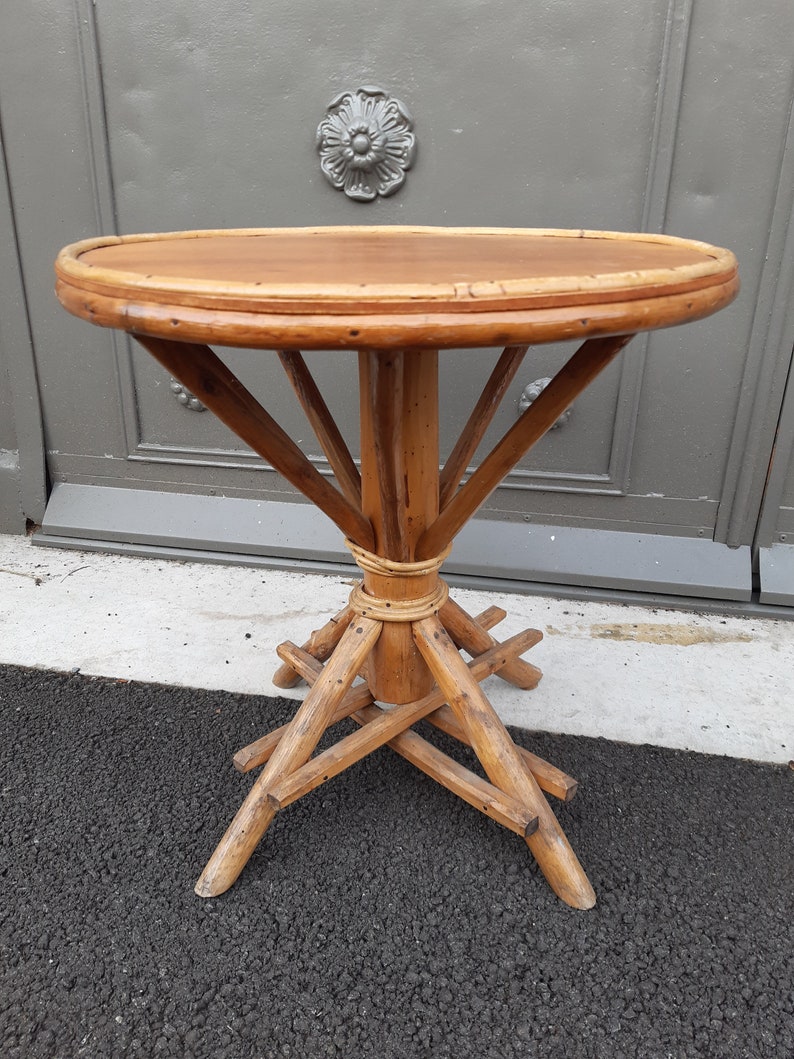 Puede incluir: Una mesa redonda de madera con una tapa tejida y una base &uacute;nica de estilo tr&iacute;pode. La mesa est&aacute; hecha de madera natural de color marr&oacute;n claro y tiene un aspecto r&uacute;stico y vintage.