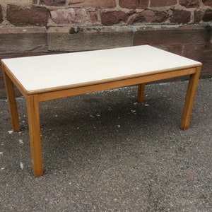 May include: A rectangular wooden table with a white laminate top. The table has a simple design with four legs and a smooth surface.