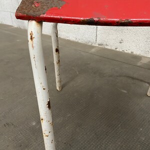 May include: A red metal chair with white painted legs. The chair is showing signs of wear and rust.