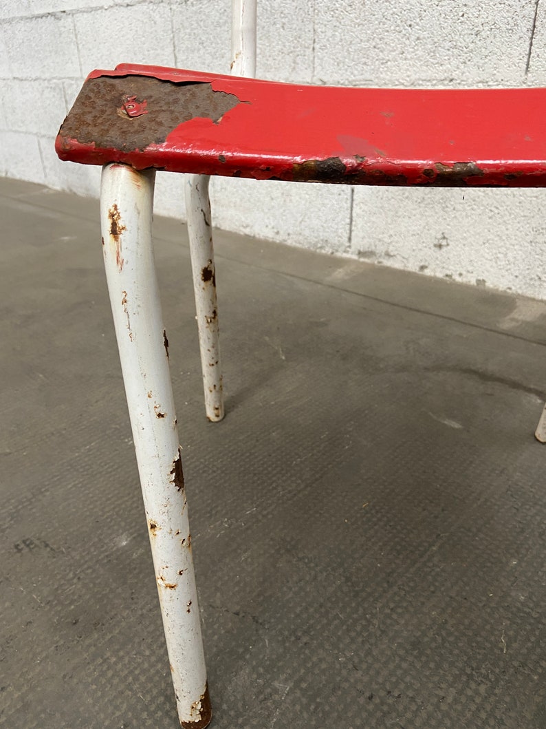 May include: A red metal chair with white painted legs. The chair is showing signs of wear and rust.