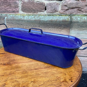 May include: A vintage blue enamel roasting pan with two handles on each end and a lid. The pan is oval shaped and has a dark blue enamel finish.