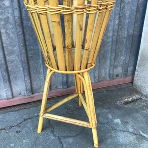 May include: A yellow bamboo plant stand with a triangular base and a round top. The stand is made of woven bamboo.