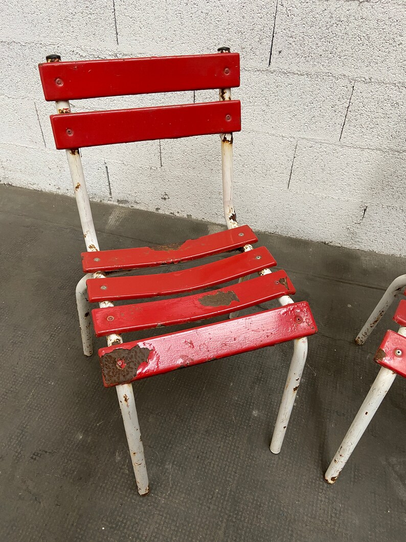 May include: Two red metal chairs with white painted legs. The chairs have a slatted seat and back. The paint is chipped and shows signs of rust.