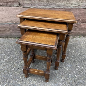 May include: A set of three wooden nesting tables with turned legs. The tables are made of dark wood and have a simple, elegant design.
