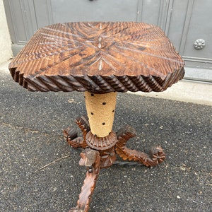 May include: A wooden side table with a square top and a carved, twisted base. The table is made of dark wood and has a natural finish. The base is decorated with a rope-like material.