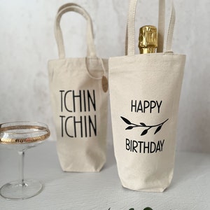 Könnte beinhalten: Zwei weiße Weintüten aus Canvas mit schwarzen Griffen. Eine Tüte sagt "Tchin Tchin" und die andere sagt "Happy Birthday" mit einem kleinen schwarzen Zweigdesign.
