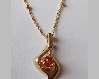 Könnte beinhalten: Eine goldene Kettenkette mit einem Anhänger in Form einer Spirale und einem kleinen orangefarbenen Edelstein.