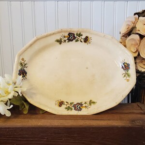 May include: A white oval serving platter with a scalloped edge and a floral design in shades of red, blue, yellow, and green.