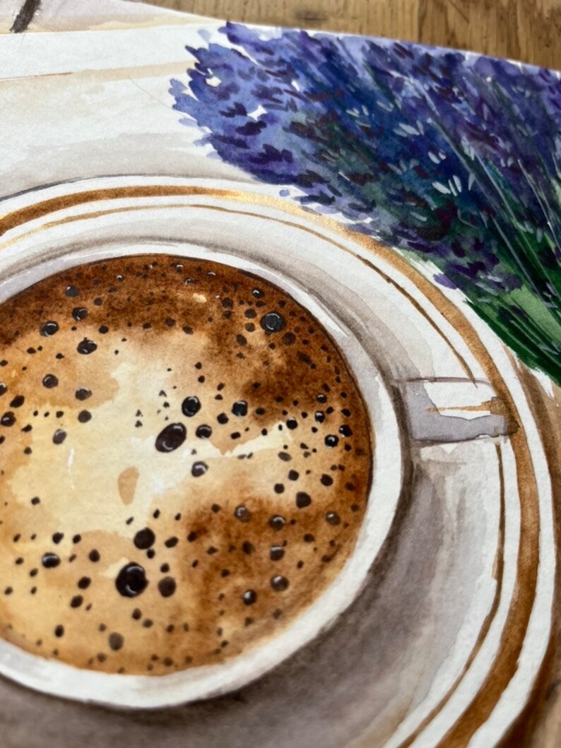 May include: A close-up of a cup of coffee with a brown frothy top. The cup is white with a gold rim and is sitting on a white saucer with a gold rim. A bouquet of lavender flowers is in the background.