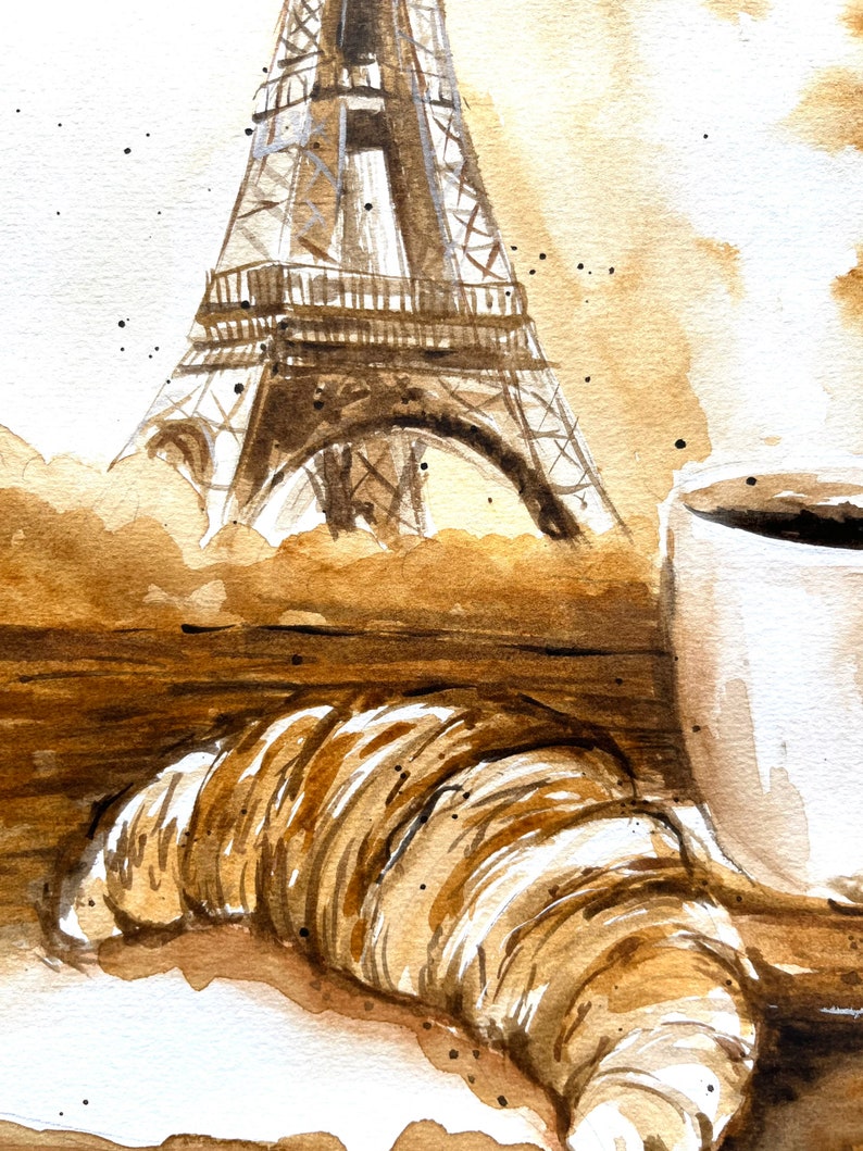 K&ouml;nnte beinhalten: Ein Aquarellbild eines Croissants, einer Tasse Kaffee und dem Eiffelturm im Hintergrund. Das Bild ist in Braun- und Wei&szlig;t&ouml;nen gehalten.