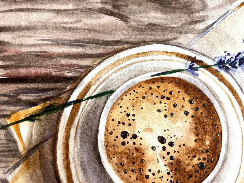 May include: A close-up of a cup of coffee with a lavender sprig on a wooden surface. The coffee is brown and has a foamy top. The lavender is purple and green.