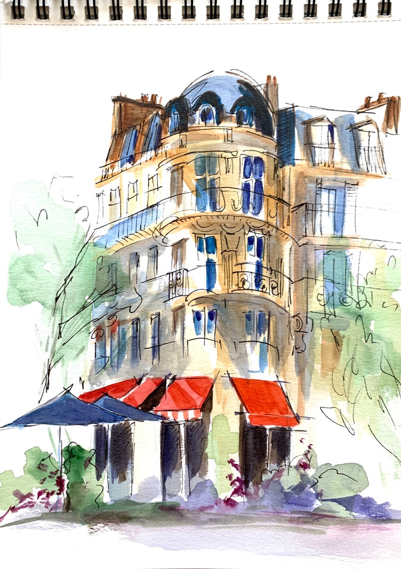 Puede incluir: Boceto en acuarela de un edificio parisino con techo abovedado y balcones. El edificio est&aacute; pintado en tonos beige y azul, con toldos rojos y una sombrilla azul delante. La obra de arte est&aacute; en un cuaderno de espiral.