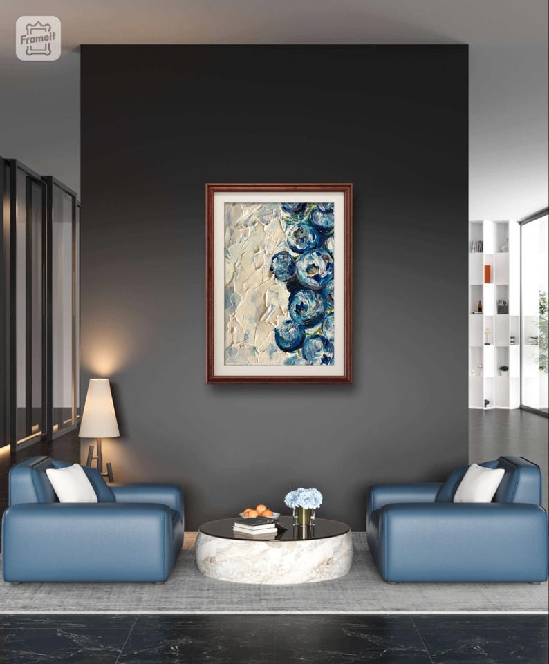 May include: A framed abstract painting with a brown wooden frame. The artwork features textured white and blue brushstrokes, depicting a cluster of blue floral shapes. The painting hangs on a dark gray wall above two blue armchairs.