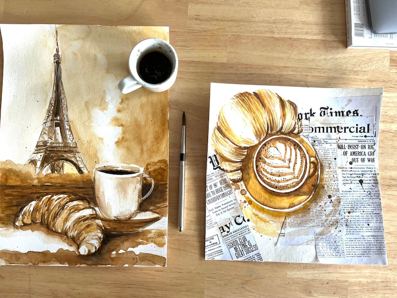 K&ouml;nnte beinhalten: Ein Aquarellbild einer Pariser Szene mit dem Eiffelturm, einem Croissant und zwei Tassen Kaffee. Das Bild ist auf braunem Hintergrund mit einer Zeitungsstruktur gemalt.
