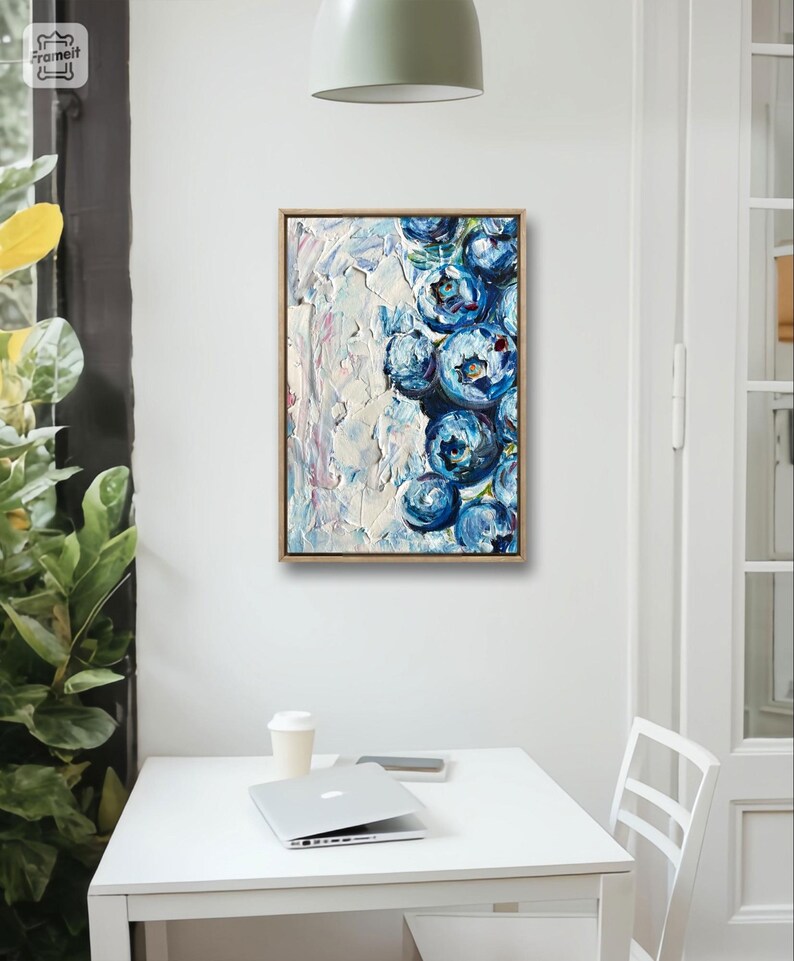 May include: An abstract oil painting of blueberries in a wooden frame. The artwork features a textured white background with a cluster of blue blueberries on the right side. The painting is displayed on a white wall above a white table.