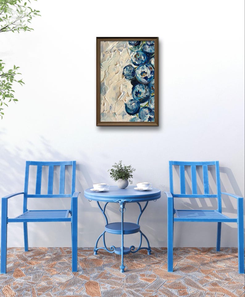 May include: An abstract painting in a brown frame, featuring blue floral shapes against a textured cream background. The painting hangs above a blue patio set with two chairs and a small round table. The table is set with two cups and a small plant.