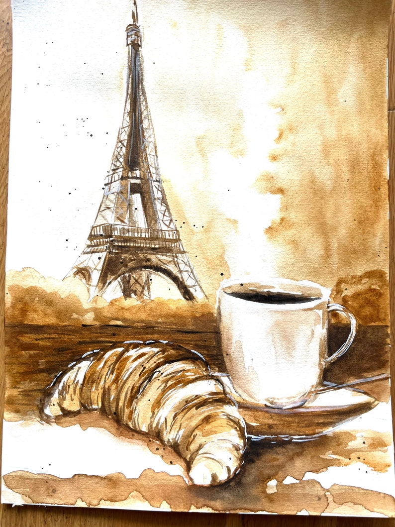 K&ouml;nnte beinhalten: Ein Aquarellbild eines Croissants, einer Tasse Kaffee und des Eiffelturms. Das Bild ist auf braunem Hintergrund mit Kaffeeflecken gemalt.
