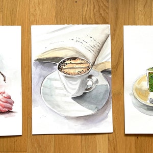 Könnte beinhalten: Drei Aquarelle, die verschiedene Speisen und Getränke darstellen. Das erste Aquarell zeigt ein Glas mit roten Himbeeren, rosa Marshmallows und roten Herzen. Das zweite Aquarell zeigt eine Tasse Kaffee mit einem Buch im Hintergrund. Das dritte Aquarell zeigt ein Stück grünes Gebäck mit einer Tasse Kaffee und einer Gabel.