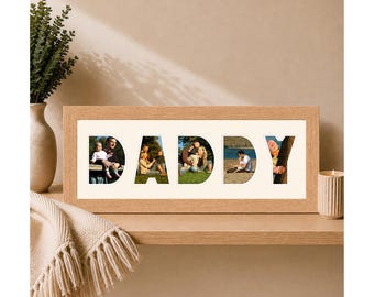 May include: A rectangular light wood picture frame containing a white mat with five cutouts in the shape of the letters D, A, D, D, and Y. Each letter cutout displays a different photograph of people interacting outdoors in various settings.