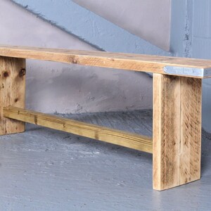 May include: A rustic wooden bench with a natural wood finish and metal accents. The bench has a simple design with a rectangular seat and two legs on each side. The bench is made from reclaimed wood and has a distressed look.