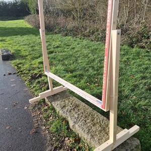 May include: A wooden frame with a red and white label that reads "Regular Carpet Gripper" and "Regular Carpet Gripper". The frame is standing on a stone surface with grass in the background.
