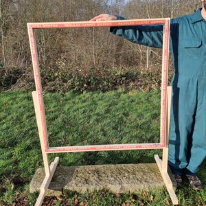 May include: A wooden frame with a red and white tape border that says "REGULAR CARPET GRIPPER" around the perimeter. The frame is standing on a stone surface.