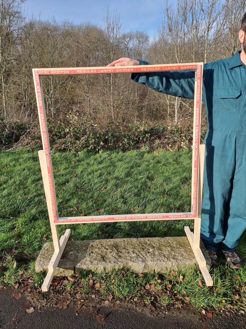 May include: A wooden frame with a red and white tape border that says "REGULAR CARPET GRIPPER" around the perimeter. The frame is standing on a stone surface.