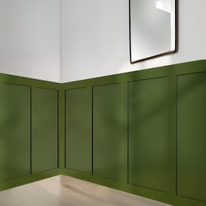May include: A room with a light wood floor and green wainscoting. A woven light fixture hangs from the ceiling. A rectangular mirror with a dark wood frame hangs on the wall.