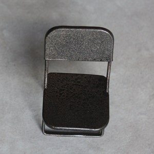 May include: A small, black metal folding chair with a textured finish. The chair is made of thin metal and has a simple design.