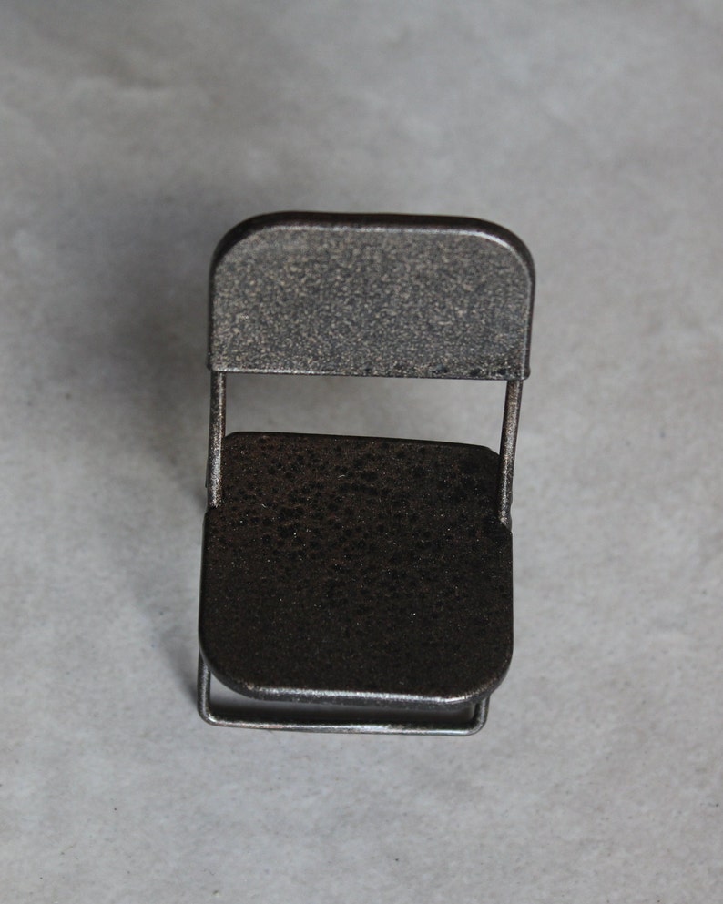 May include: A small, black metal folding chair with a textured finish. The chair is made of thin metal and has a simple design.