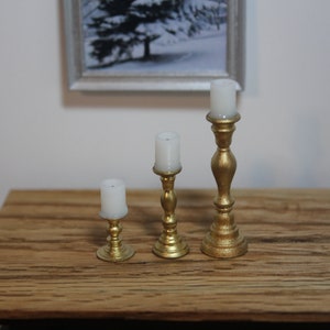 Peut inclure: Trois bougeoirs dorés avec des bougies blanches. Les bougeoirs sont de tailles différentes et ont un design classique.