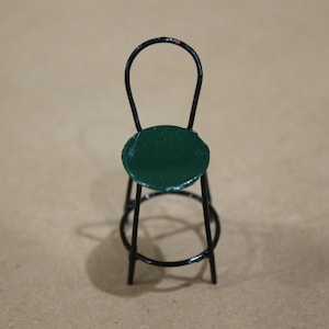 May include: A miniature black metal chair with a green round seat.