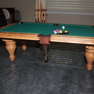 Könnte beinhalten: Ein Miniatur-Billardtisch mit grünem Filzspielfeld und Holzbeinen. Der Tisch hat eine braune Filzverkleidung an den Rändern und einen Satz bunter Billardkugeln auf dem Tisch.