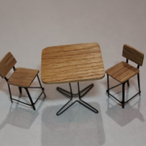 May include: A miniature wooden table set with two chairs. The table and chairs have a light brown wood finish and black metal legs.