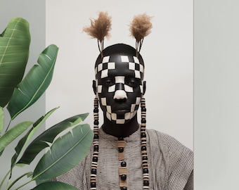 May include: A person with black and white checkered face paint wears a brown and white patterned shirt with a long beaded necklace. The person has brown hair styled in two small buns.