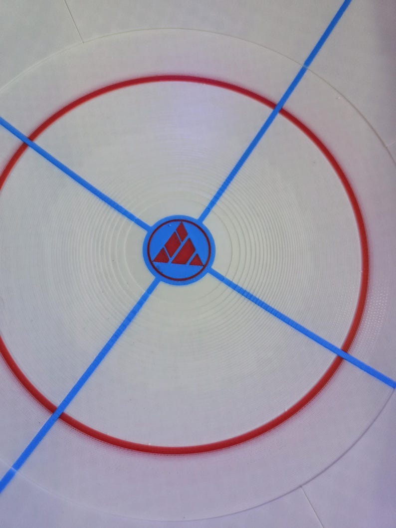May include: Circular white object with a red ring and blue lines radiating from the center. A blue circle with a red triangle design is in the center. The object has a textured surface.