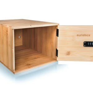 May include: A light brown bamboo box with an open front and a hinged door. The door is open, revealing the interior. The door has a black combination lock and the word "surebox" printed on it.