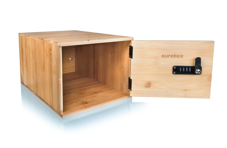 May include: A light brown bamboo box with an open front and a hinged door. The door is open, revealing the interior. The door has a black combination lock and the word "surebox" printed on it.