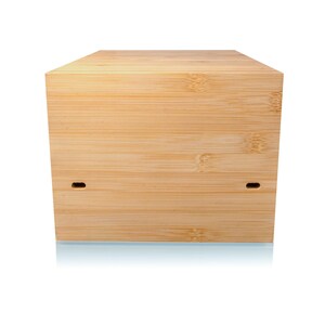May include: A light-colored, rectangular bamboo box with a natural wood grain finish. The box has two small, rectangular cutouts on the front. The box is sitting on a reflective surface.