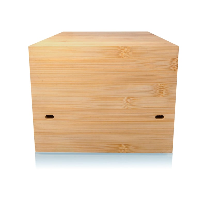 May include: A light-colored, rectangular bamboo box with a natural wood grain finish. The box has two small, rectangular cutouts on the front. The box is sitting on a reflective surface.