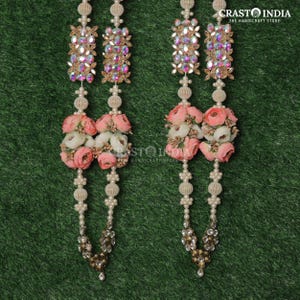 May include: Two decorative garlands with floral and beaded elements. Each garland features clusters of pink and white flowers, iridescent gems, and pearl-like beads. The garlands are suspended against a green background.