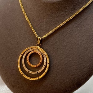 Può includere: Una collana d'oro con un ciondolo che presenta tre cerchi concentrici. I cerchi sono realizzati in diverse tonalità d'oro, creando un effetto a strati.