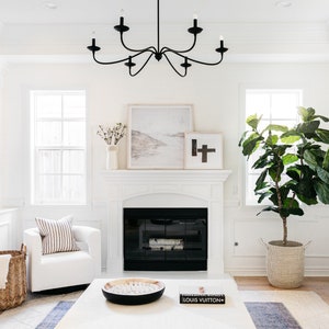 May include: A white living room with a fireplace, a white armchair, a large potted plant, and a white coffee table with a black bowl and a book that says "LOUIS VUITTON".