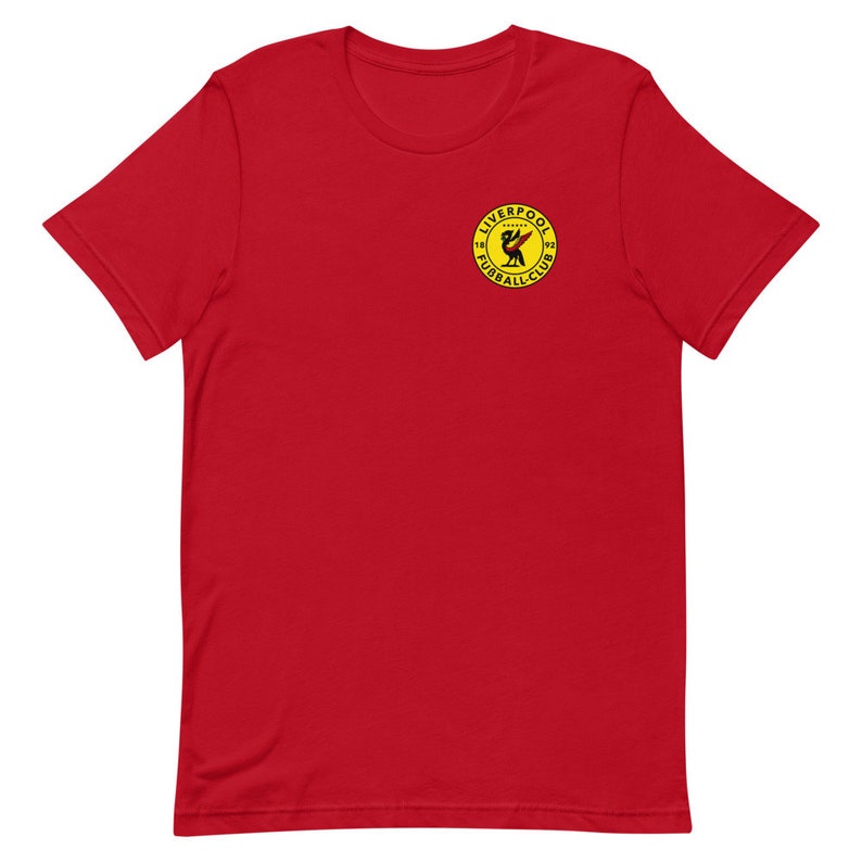 May include: Red short-sleeved t-shirt with a yellow circle logo featuring a black bird and the text "Liverpool Football Club 1892".