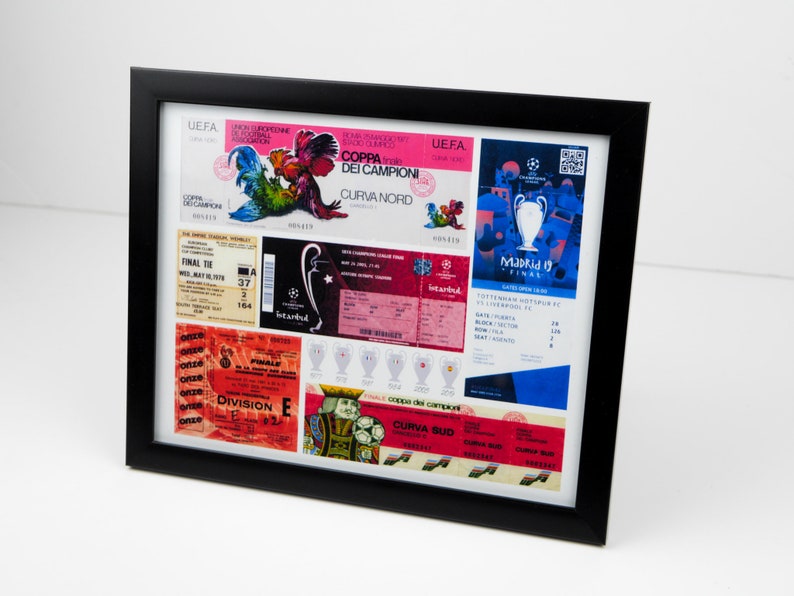 May include: A framed collage of vintage soccer tickets and memorabilia. The tickets are from different games and leagues, including the UEFA Champions League and the Coppa dei Campioni. The memorabilia includes a rooster logo and a trophy. The frame is black and the background is white.