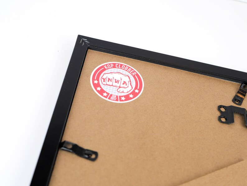 May include: Black picture frame with a red and white sticker that says "Kop Clobber" with a fist graphic and the year 2017.