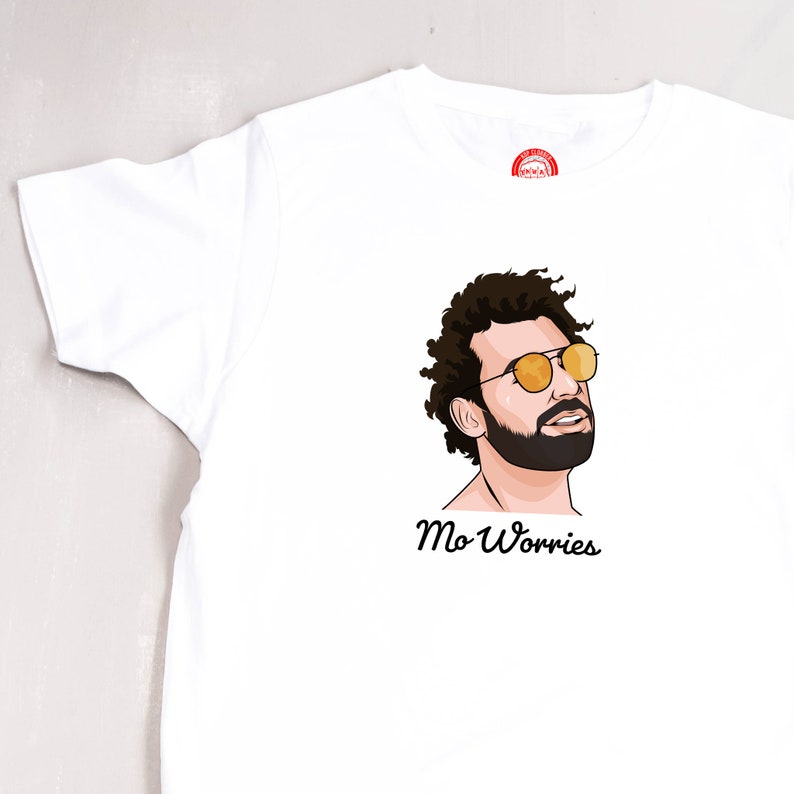May include: White t-shirt featuring a cartoon illustration of a man with curly hair wearing sunglasses and a beard. The text "Mo Worries" is printed below the illustration.