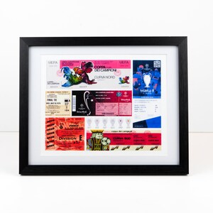 May include: A framed collage of vintage soccer tickets and memorabilia. The tickets are from different games and leagues, including the UEFA Champions League and the Coppa dei Campioni. The memorabilia includes a small replica of the Champions League trophy and a few other items.