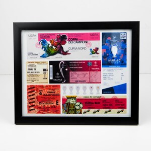 May include: A framed collage of vintage soccer tickets and memorabilia. The tickets are from different European teams and tournaments, including the UEFA Champions League and the Coppa dei Campioni. The collage also includes a small trophy and a rooster graphic.