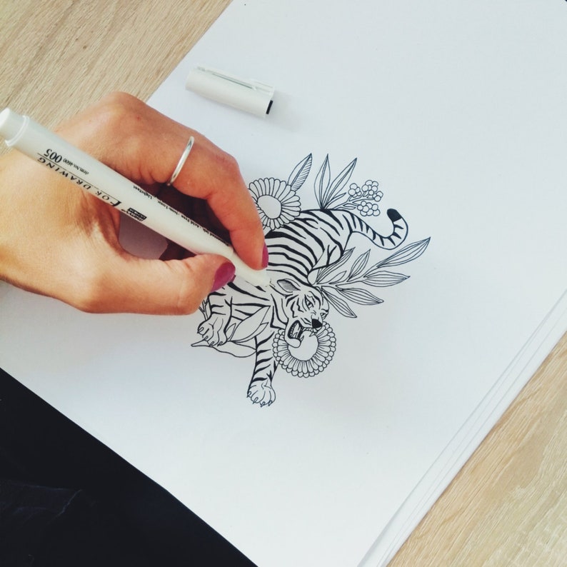 May include: A black and white line drawing of a tiger with floral accents. The tiger is drawn in a stylized, almost cartoonish style, with a fierce expression. The flowers are delicate and intricate, adding a touch of whimsy to the design.